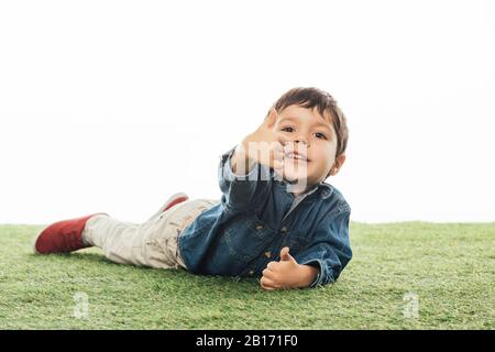 cute and smiling boy showing like and lying on grass isolated on white Stock Photo