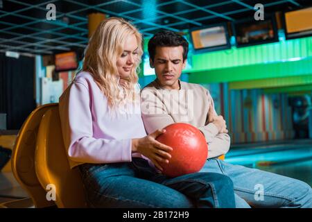 smiling girl showing bowling ball to thoughtful boyfriend in bowling club Stock Photo