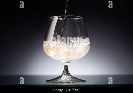 whiskey pouring into transparent glass with ice in dark with back light Stock Photo