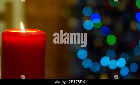 One large red burning candle on abstract blurred background with big circular colourful bokeh Stock Photo