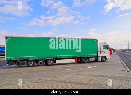 In the foreground a truck with a semi-trailer. Green tarpaulin. A row of trucks in a parking lot. Stock Photo