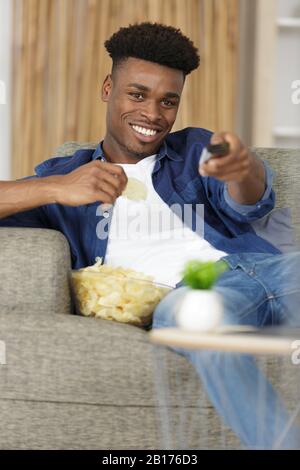 young man watching tv and eating chips Stock Photo