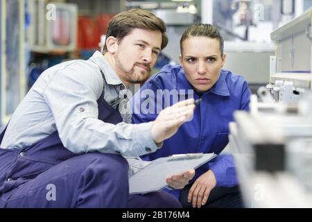 man explains woman how to use a machine in factory Stock Photo
