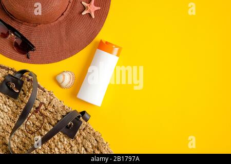 Sunscreen cream bottle mockup, rattan bag, beach hat, female sunglasses and seashells on yellow background. Sun protection and beach skin care concept Stock Photo