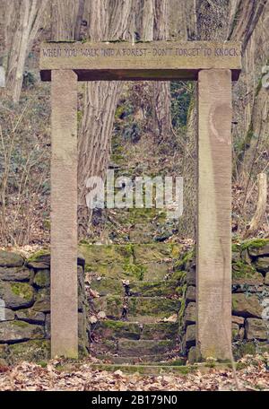 Old stone door structure in the middle of the woods. On the lintel is written 'When you walk into a forest, don't forget to knock'. Stock Photo