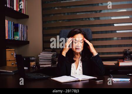 Portrait of a senior woman in her business office with hands on head looking at her notebook Stock Photo