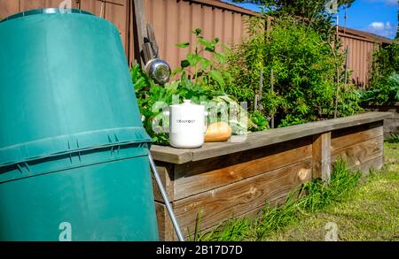 Kitchen waste collection pot outside on wall of raised vegetable bed next to compost bin, recycling domestic organic kitchen waste into compost Stock Photo