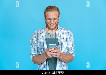 Smiling young man use modern smart phone smile text message chat online Stock Photo