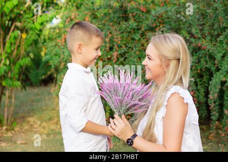 Happy mothers day. Son giving flowers to mom outside isolated green foliage background Stock Photo