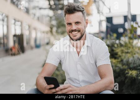Young smiling man using smartphone and looking at camera Stock Photo