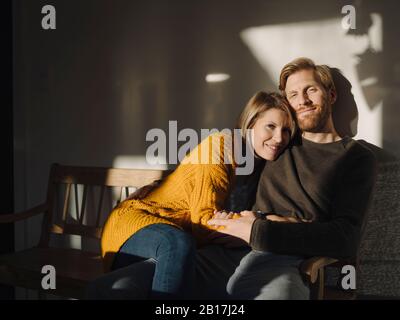 Portrait of smiling couple sitting on bench in sunlight at home Stock Photo