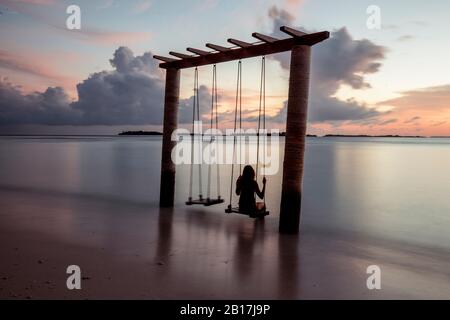 Woman on a swing at the sea at sunset, Maguhdhuvaa Island, Gaafu Dhaalu Atoll, Maldives Stock Photo