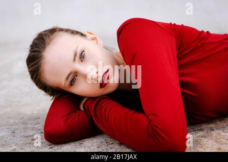 Portrait of young woman dressed in red lying on the ground outdoors Stock Photo
