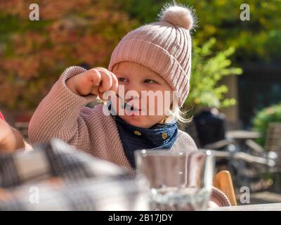 Portrait of toddler girl eating at outdoor cafe in autumn Stock Photo