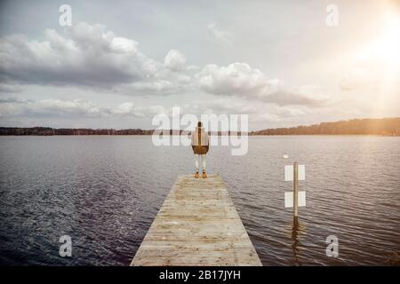 Back view of young man standing on a jetty looking at lake Stock Photo