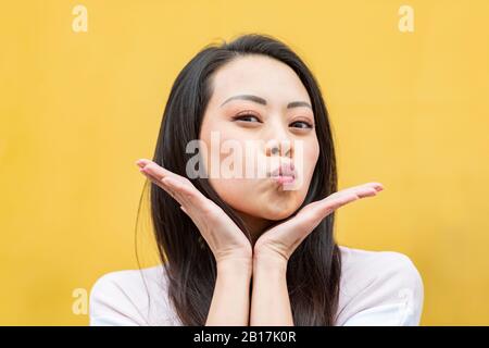 Portrait of woman against yellow background pouting mouth Stock Photo