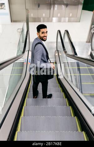 Portrait of smiling young businessman on escalator turning round Stock Photo