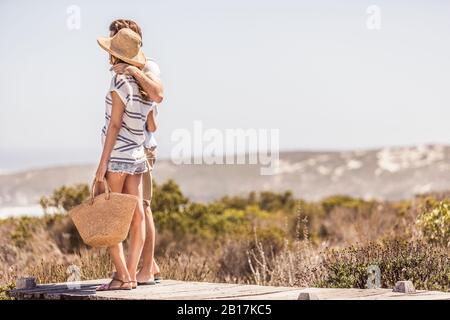 Young couple standing on a boardwalk at the coast looking at view Stock Photo