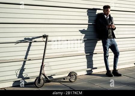 Man with smartphone and e-scooter outdoors Stock Photo