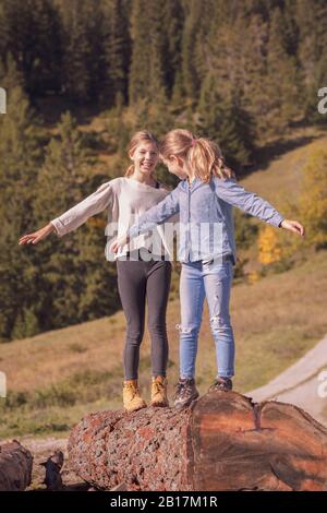 Two young girls balancing on a tree trunk