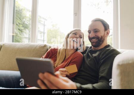 Couple sitting at home on couch, using digital tablet Stock Photo