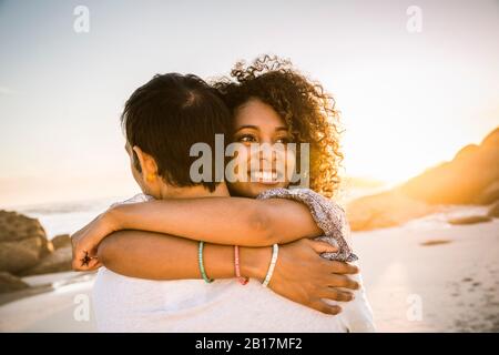 Happy couple hugging on the beach at sunset Stock Photo