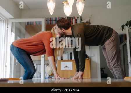 Couple standing on chairs, kissing, leaning on dining table Stock Photo