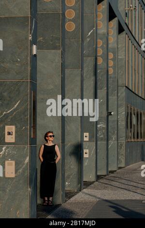 Red-haired woman with sunglasses, leaning on pillars in the city Stock Photo
