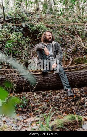Young man in forest, sitting on tree trunk Stock Photo