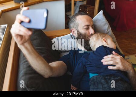 Man taking a selfie with his cute sleeping son on the sofa Stock Photo