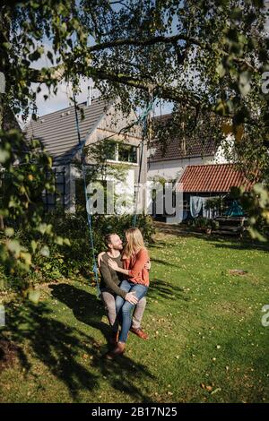 Affectionate couple sitting on swing in in their garden Stock Photo