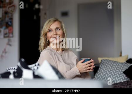 Smiling blond woman relaxing at home sitting on couch Stock Photo