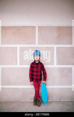 Portrait of smiling boy wearing helmet holding skateboard at a wall Stock Photo