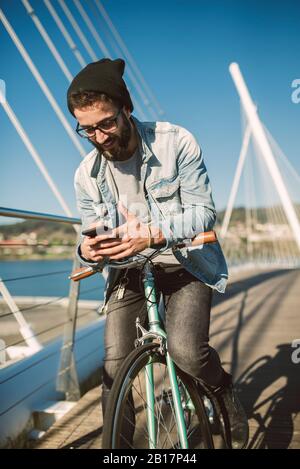 Young man commuting in the city with his fixie bike, using smartphone Stock Photo