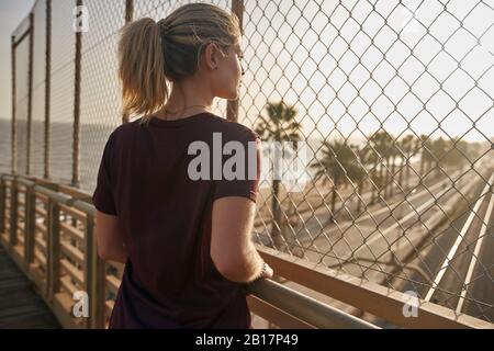 Sporty young woman standing on a bridge looking through a fence Stock Photo