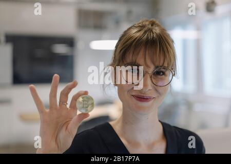 Portrait of businesswoman holding bitcoin in office Stock Photo