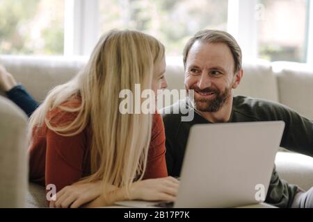 Couple sitting at home on couch, using laptop Stock Photo
