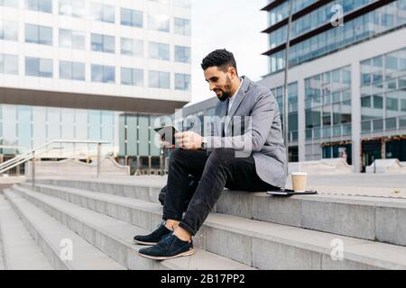 Casual young businessman sitting on stairs in the city using tablet Stock Photo