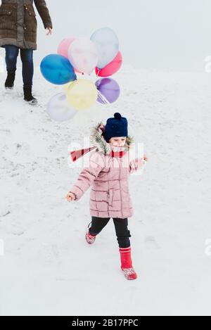 Little girl with ballons running down a hill in winter Stock Photo