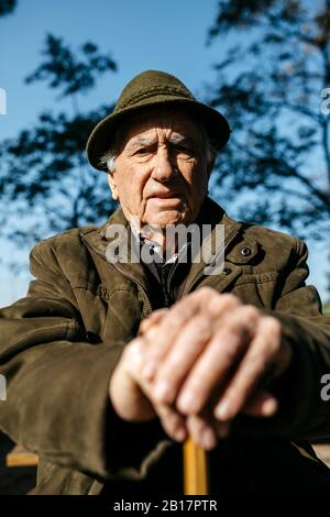 Old man with cane sitting on banch in a park Stock Photo