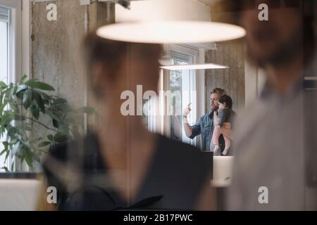 Casual businessman carrying little daughter at the window in office Stock Photo