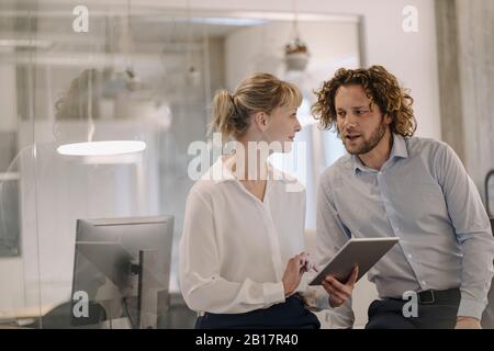 Businessman and businesswoman with tablet talking in offce Stock Photo