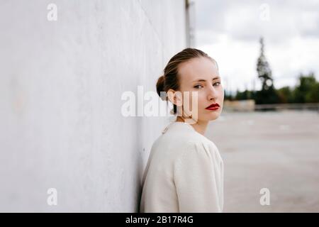 Portrait of serious young woman with red lips leaning against wall Stock Photo