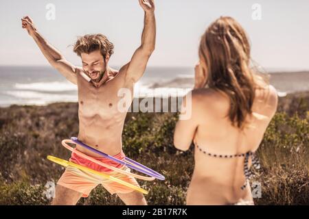 Woman looking at young man playing with hoola hoop Stock Photo