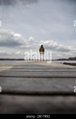Back view of young man standing on a jetty looking at lake Stock Photo
