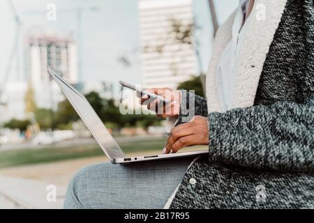 Casual businesswoman sitting in the city, using laptop, close up Stock Photo