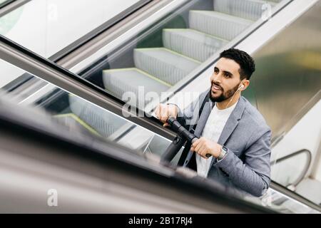 Smiling young businessman with electric scooter on escalator Stock Photo