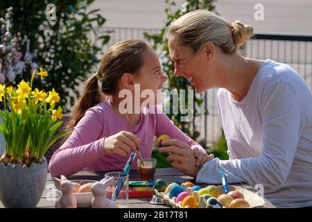 Happy mother and daughter painting Easter eggs at garden table having fun Stock Photo