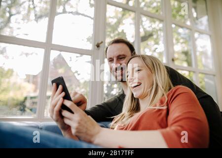 Laughing couple using smartphone at home Stock Photo