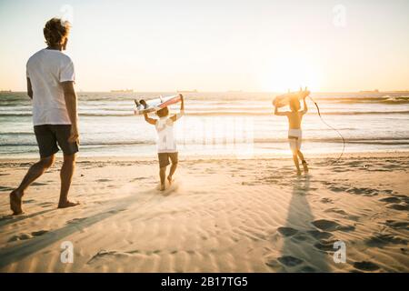 Father and two sons with surfboards walking on the beach at sunset